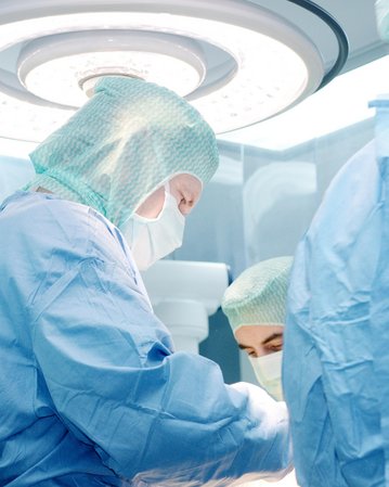 Chirurgisches Team in Schutzkleidung führt einen Eingriff in einem Operationssaal durch, umgeben von medizinischen Geräten und Beleuchtung.