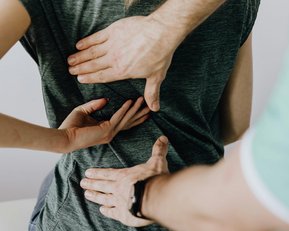 Eine Person erhält eine Rückenmassage von einem Therapeuten, der beide Hände auf den unteren Rücken der Person platziert hat.